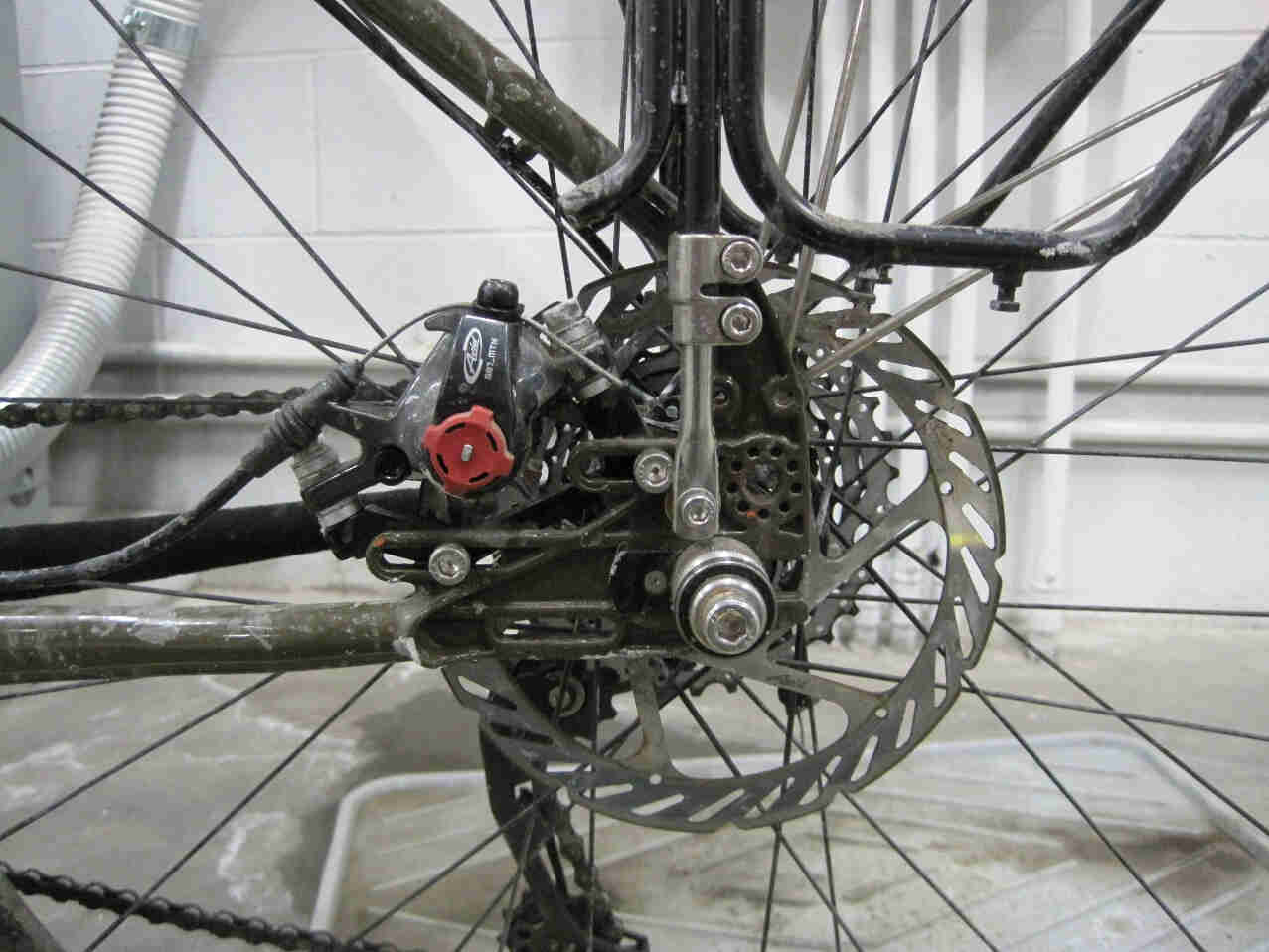 Left side view of the rear brakes disc and caliper on a Surly Troll bike, on a cement floor inside a warehouse